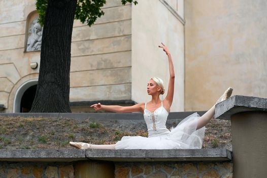 Beautiful young ballerina doing splits outdoors wearing dramatic white dancing outfit beauty fashion sensuality concept.