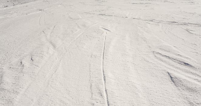 Slope covered with crystalline snow, few trails from ski visible.