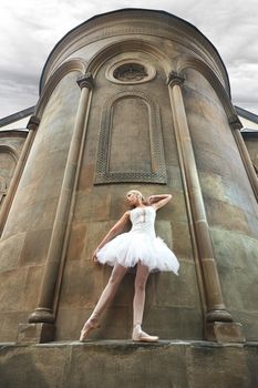 Low angle shot of a graceful ballerina posing elegantly on the wall of a big old castle outdoors.