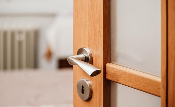 Opened modern wooden door into room, closeup detail on metal handle.