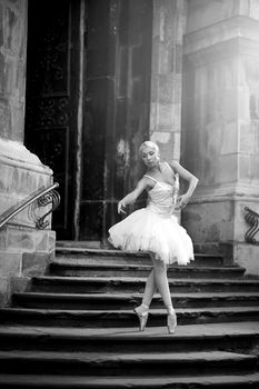 Dancing at any place. Portrait of a beautiful blonde female ballet dancer on an old stairway monochrome shot