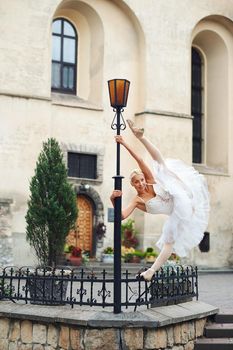 Shot of a flexible professional ballet dancer performing outdoors in the city doing splits near street lamp smiling joyfully stretching flexibility beauty art performance.