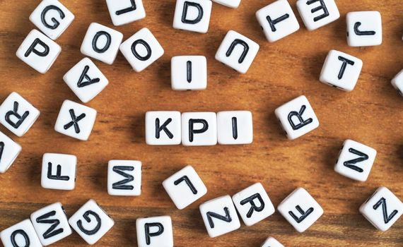 Small white and black bead cubes on wooden board, letters in middle spell KPI - Key Performance Indicators concept.