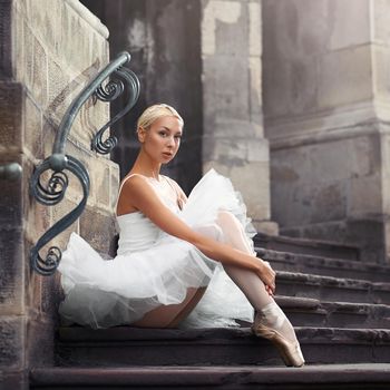 Looking thorough you. Portrait of a young ballerina sitting on an old stairway outdoors with her arms around her knees