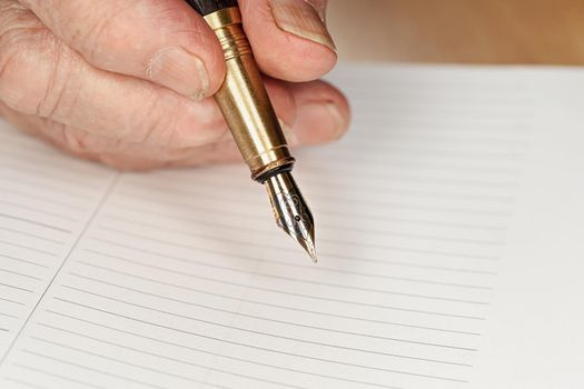 Gold coloured fountain ink pen in senior woman hand about to write something on empty daily planner page, closeup detail.