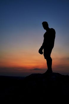 Silhouette of a man standing on top of a rock observing beautiful sunset copyspace anonymous mysterious nature skies sky dusk epic alone person loneliness beauty relaxation vitality harmony.