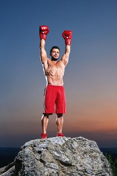 Vertical shot of a victorious male fighter celebrating winning his fight with his arms raised to the air epic sunset on the background winner happiness lifestyle fighting boxing gloves champion victory.