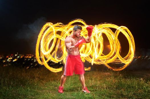 Horizontal full length shot of a powerful forceful young male boxer posing in a fighting stance outdoors fire and flames on the background copyspace power strength sports motivation athlete lifestyle .