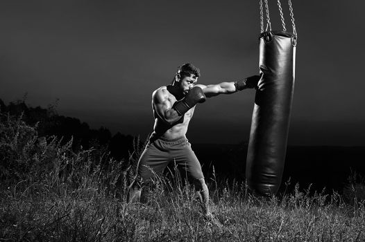 Monochrome shot of an aggressive young boxer hitting punching bag training outdoors copyspace masculinity nature fitness sports athlete athletics activity lifestyle body muscular toughness combat
