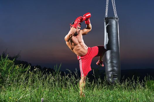 Professional male fighter working out outdoors kicking a punching bag with his knee copyspace kickboxing Muay Thai martial arts combat kick fighting training sports fitness muscles ripped body torso .
