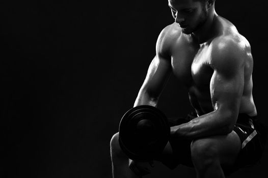 Black and white shot of a strong young muscular athlete exercising with dumbbells strengthening his biceps copyspace brutality confidence masculinity concentration focusing gym sports body muscles.