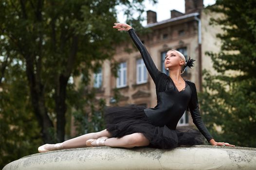 Gorgeous young ballerina wearing black swan dancing outfit posing elegantly outdoors looking away.