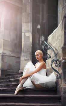 Looking unprotected. Young attractive ballet dancer sitting on the stairs embracing her knees soft focus