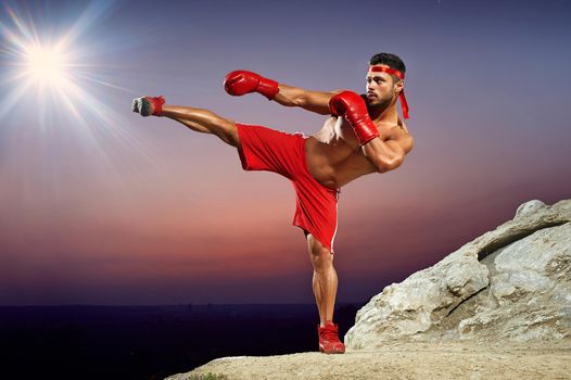 man with a naked torso, muscles, developed muscles, muscular body, athlete, boxer in training on the hillside at sunset, evening workouts, side kick, red boxing gloves, red boxing form.