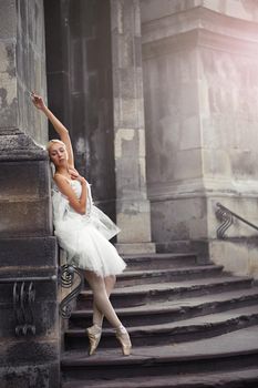 Vertical full length shot of a gorgeous ballerina leaning on the wall of an old castle posing gracefully on the stairs.