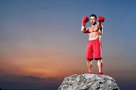 Horizontal full length shot of a professional male boxer wearing boxing gloves posing confidently outdoors training practicing punching working out preparing powerful fitness sports sportsman fighter.