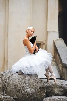 Vertical portrait of a gorgeous young ballerina sitting outdoors in the city with a black cat in her arms animals comfort love friendship pets sensuality loneliness beauty harmony concept.