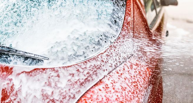 Detail on car rear window covered with soap foam, more spraying from brush, when washed in carwash.