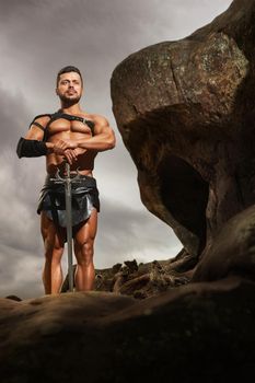 On guard of peace. Vertical full length shot of a muscular warrior standing with a sword on a rock looking away