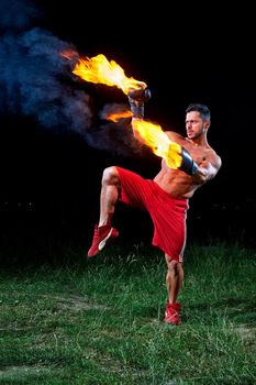 Vertical shot of a muscular aggressive fighter with burning boxing gloves training outdoors at night fire fiery flaming burn power strength sports fierce masculinity motivation effort energy.