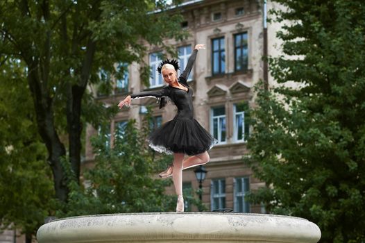 Horizontal shot of a professional ballerina wearing black dress dancing outdoors in the street of an old town.