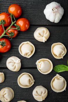 Tasty raw tortellini with flour and basil set, on black wooden table background, top view flat lay