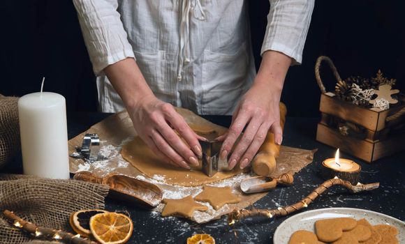 Christmas and new year celebration cooking table with woman hands prepairing gingerbread cookies dow, decor, candle, dry oranges, stars shape tool