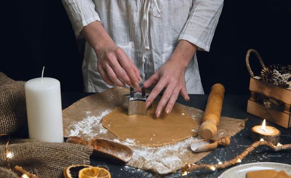 Christmas and new year celebration cooking table with woman hands prepairing gingerbread cookies dow, decor, candle, dry oranges, stars shape tool