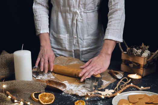 Christmas and new year celebration cooking table with woman hands prepairing gingerbread cookies dow, decor, candle, dry oranges, stars shape tool