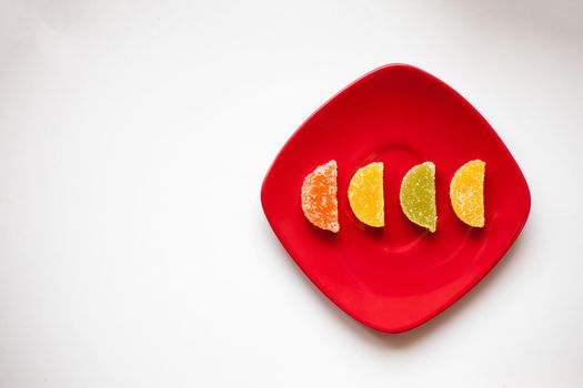 Four Sugar candies. Coloured green, yellow, orange. Shaped as half moon. One red plate.