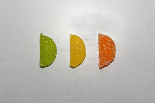 Three Sugar candies in a row. Green, yellow, orange. In a shape of half moon. Sorted in a row.