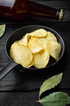 Salty potato chips snack set, and bottle of beer, on black wooden background