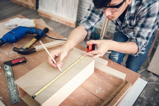 Carpenter Man is Working Timber Woodworking in Carpentry Workshops, Craftsman is Using Tape Measure to Measuring Timber Frame for Wooden Furniture in Workshop. DIY Workmanship, Job Occupation Concept.