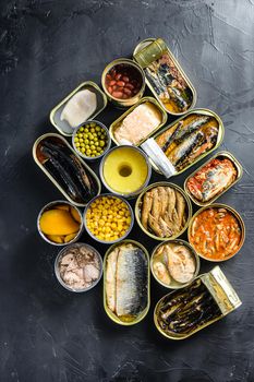 Canned conserve products in tin cans. with fresh organic ingridients Saury, mackerel, sprats, sardines, pilchard, squid, tuna pinapple, corn, peas, mango , beans, over black stone textured background topview concept.