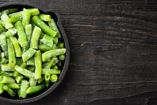 Frozen cut green beans vegetable set, in frying cast iron pan, on black wooden table background, top view flat lay, with copy space for text
