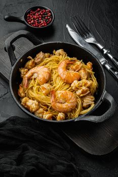 Pesto prawn pasta served, in cast iron frying pan, on black stone background