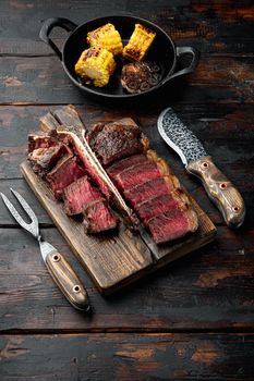 Medium rare dry aged beef steak grilled and sliced set, t bone or porterhouse cut, on wooden serving board, on old dark wooden table background, with copy space for text