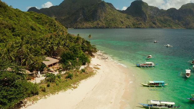 aerial view tropical beach on island with palm trees, blue lagoon and azure clear water. Helicopter Island in El Nido, Palawan Philippines. Tropical landscape with blue lagoon, coral reef