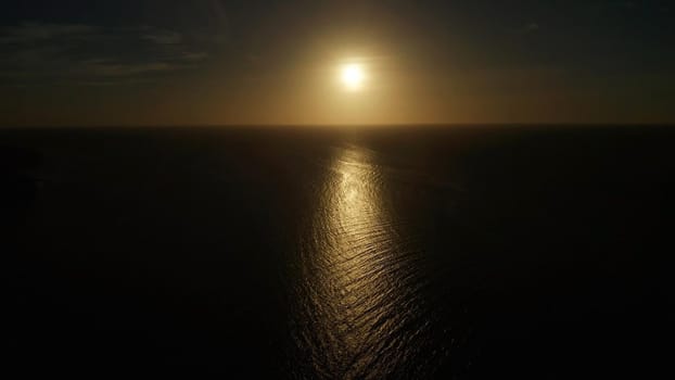 Sunset above the sea surface with waves, aerial drone. Reflected sun on a water surface. Sunset over ocean. Seascape, Summer and travel vacation concept