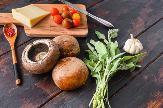 Portabello mushrooms ingredients for baking, cheddar cheese, cherry tomatoes and sage on old dark wood background, side view