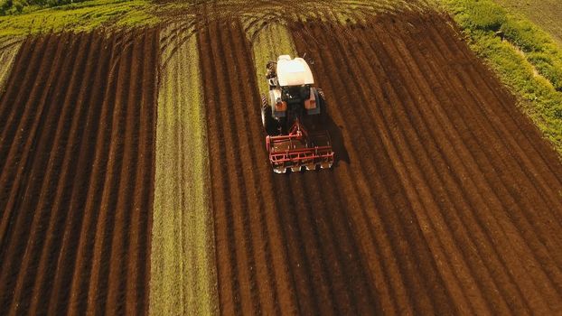 Farmer in tractor preparing land with seedbed cultivator in farmlands. Tractor plows a field. Agricultural work in processing, cultivation of land. Farmers preparing land and fertilizing. Agricultural workers with tractors.