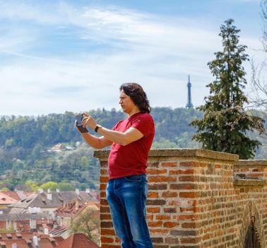 A man stands on a brick wall and photographs the panorama of Prague. Journey