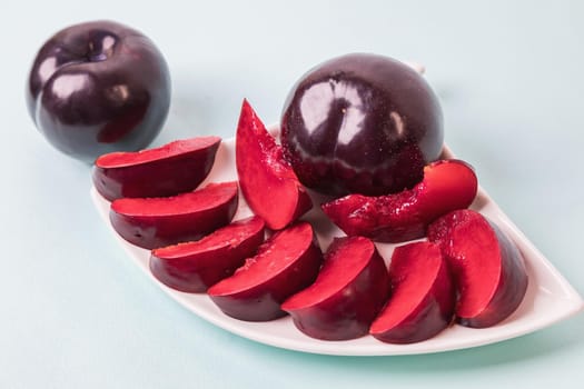 On a white saucer there is a large plum cut into wedges, next to it there are two more plums. The pulp of red berries. Close-up.