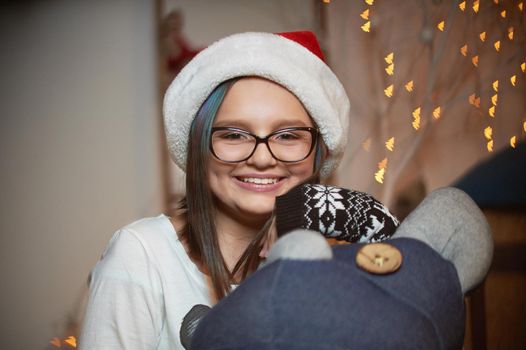 Christmas is all smiles. Closeup of a joyful young girl in a Santa Claus hat smiling to the camera relaxing at home on Christmas eve soft focus and noise