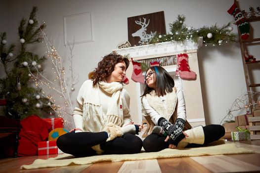 Mother daughter time. Beautiful mother and daughter sitting together on the floor near the Christmas tree looking at each other smiling warmly soft focus and noise