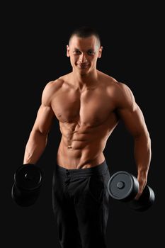 Tuned body. Studio portrait of a young handsome fitness man posing with a dumbbell showing off his stunning muscled torso on dark background