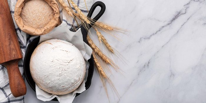 Fresh raw homemade yeast dough resting in cast iron skillet on marble table flat lay.