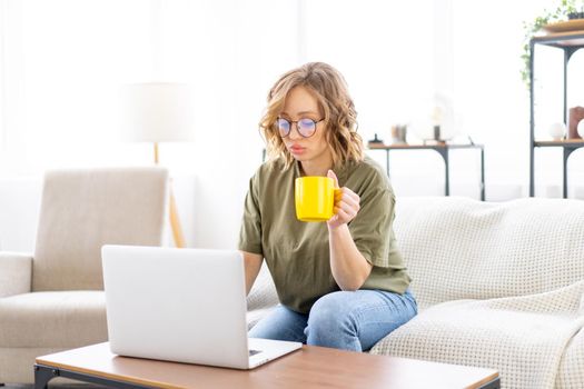 Woman with glasses use laptop typing keyboard sitting couch big window background home interior Freelance female working from home Distance learning student relaxing watch lessons video conference.