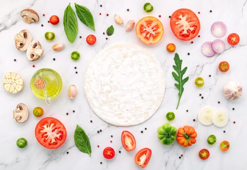 The ingredients for homemade pizza set up on white marble background.