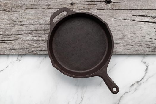 Empty old cast iron skillet set up on white marble  background with flat lay and copy space.